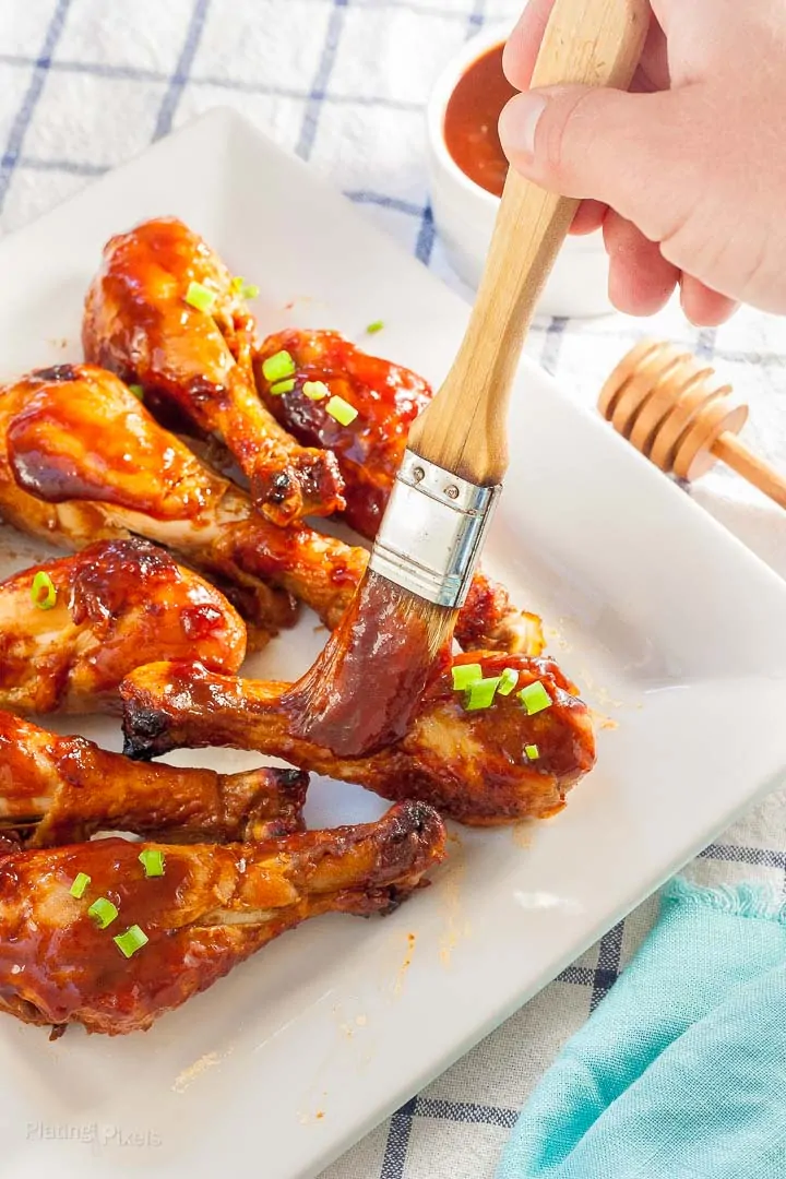 Hand brushing a bbq glaze over Easy Honey BBQ Oven Baked Chicken Drumsticks
