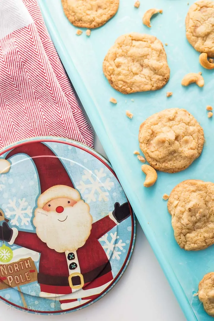 Chewy Cashew Toffee Cookies on teal cookie sheet with a santa decorated cookie tin beside it