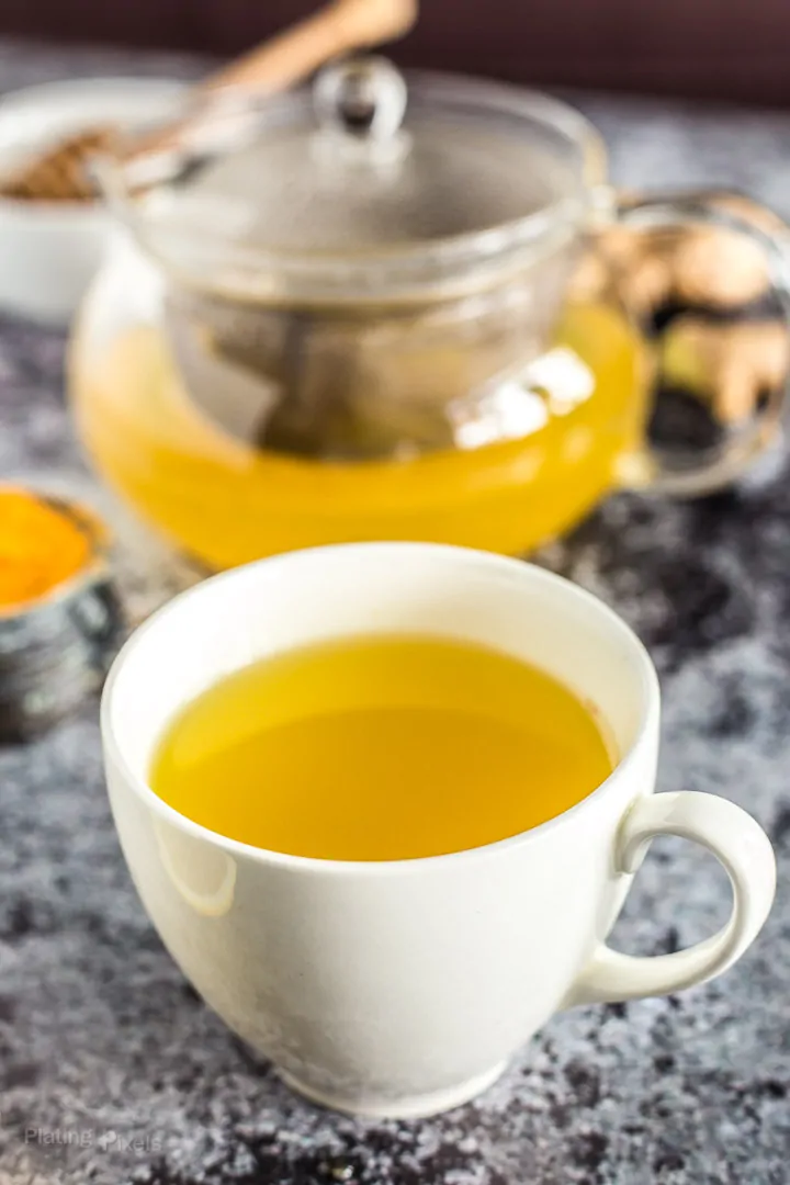 Cup of homemade Turmeric Tea next to pot of freshly brewed tea