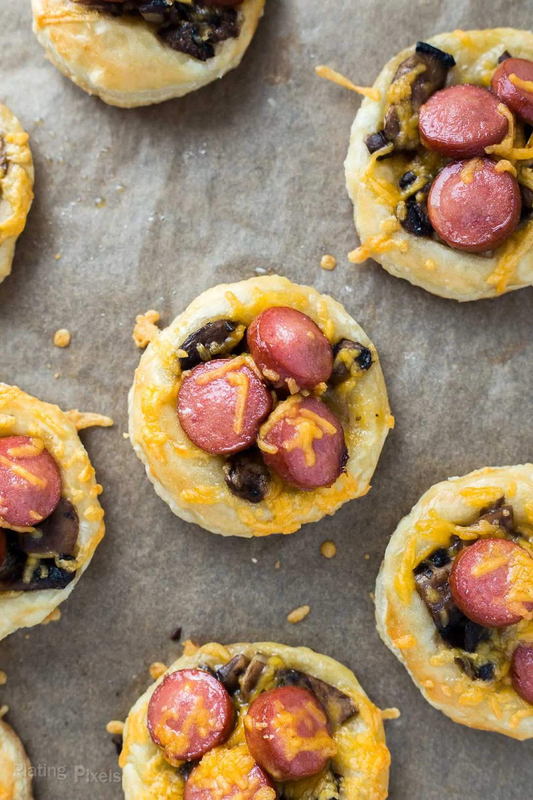 Mini pizza bites with sausage, cheese, and mushrooms on parchment paper.