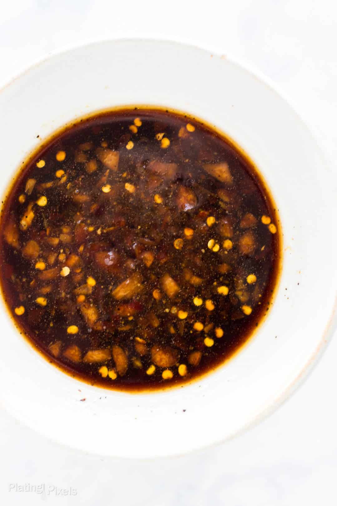 Savory soy sauce with garlic and chili flakes in a white bowl.