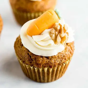 Close up of a Carrot Cake Cupcake topped with cream cheese frosting and marzipan carrot