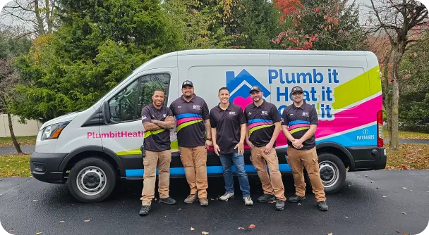 Five people in matching uniforms stand proudly in front of a "Plumb it Heat it Cool it" van, parked on a driveway with trees in the background.