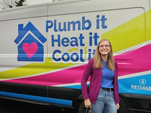A woman stands smiling in front of a van with the text "Plumb it, Heat it, Cool it" and a house logo on the side.