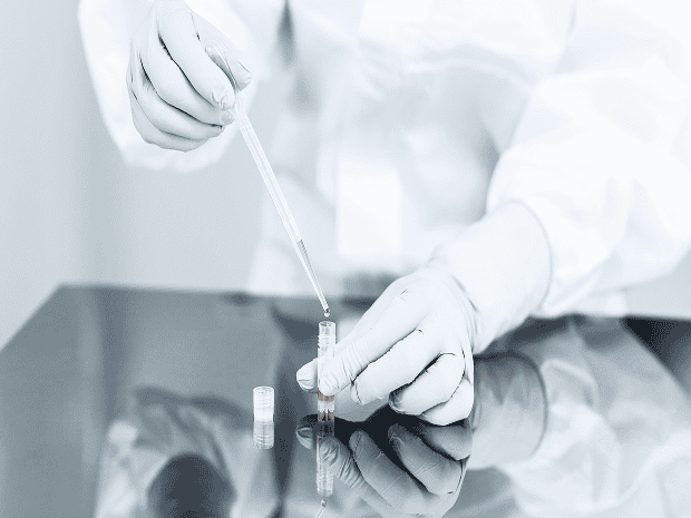 Technician in sterile PPE using a handheld particle counter to monitor air quality in a cleanroom laboratory.