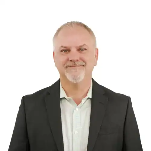 A man with short hair and a beard wearing a dark suit and light shirt, smiling at the camera.