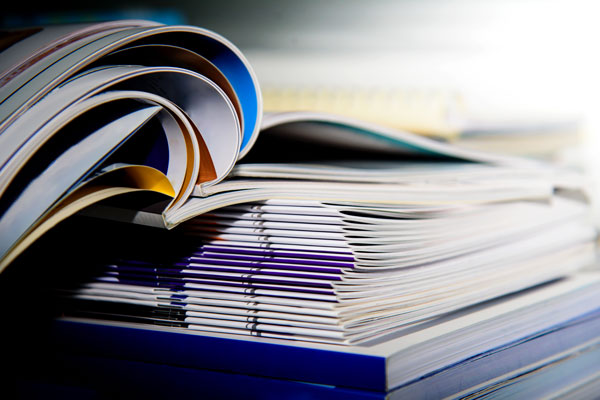 A stack of printed materials including magazines and brochures with visible pages.