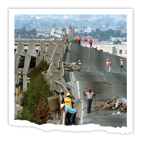 Collapsed highway section during the 1989 Loma Prieta Earthquake with workers assessing the damage.