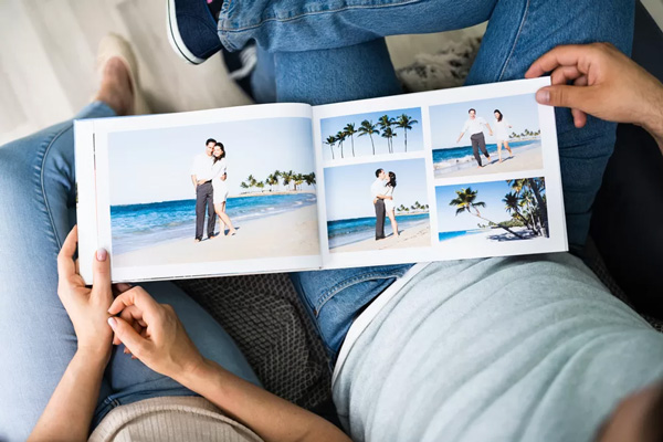 A person holding a photo book displaying images of a couple on a beach with palm trees.