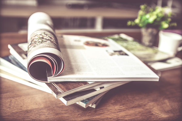 A stack of magazines with one magazine partially rolled on a wooden surface.