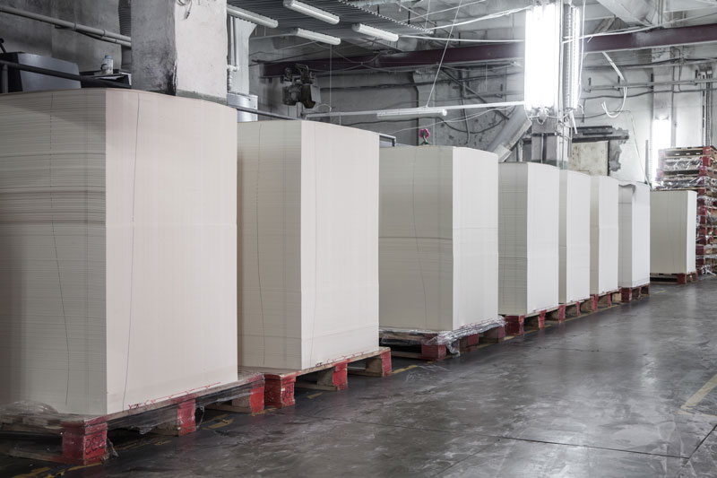 Stacks of offset commercial printing paper arranged on pallets in a warehouse setting.