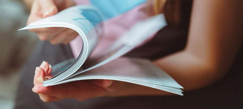 A person flipping through the pages of a magazine with visible printed content.