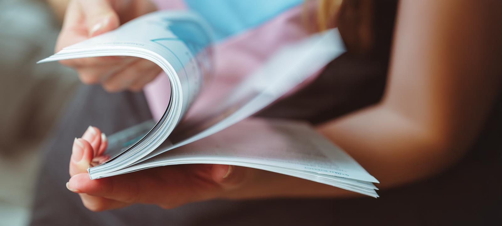 A person flipping through the pages of a magazine with visible printed content.