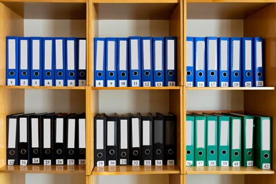 A shelf displaying various custom printed binders in black, blue, and green colors.