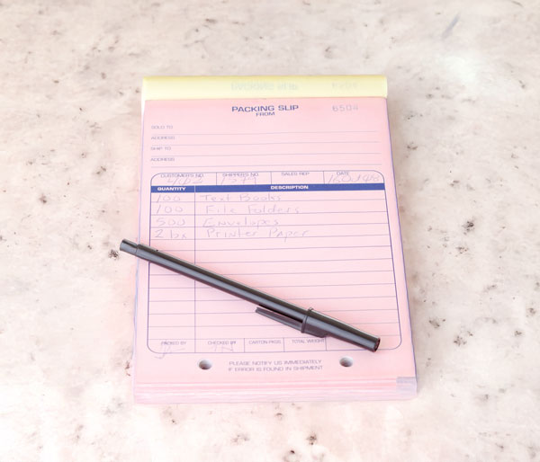 Pink carbonless form second sheet with handwritten details and a black pen on a surface.