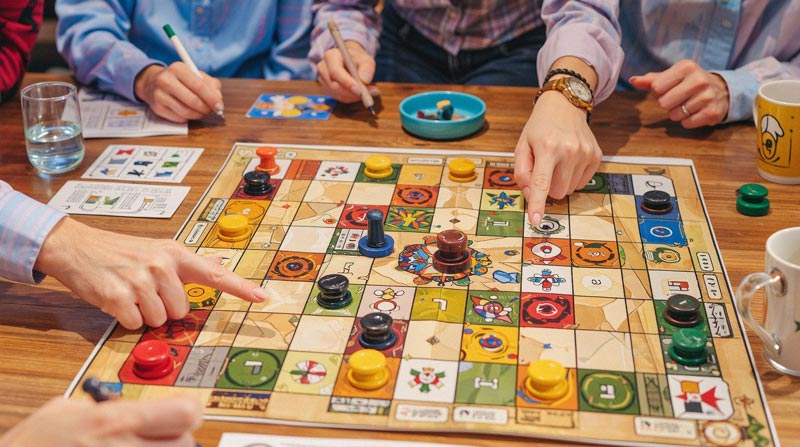 A custom gameboard featuring various colored game pieces and players' hands pointing at the board.