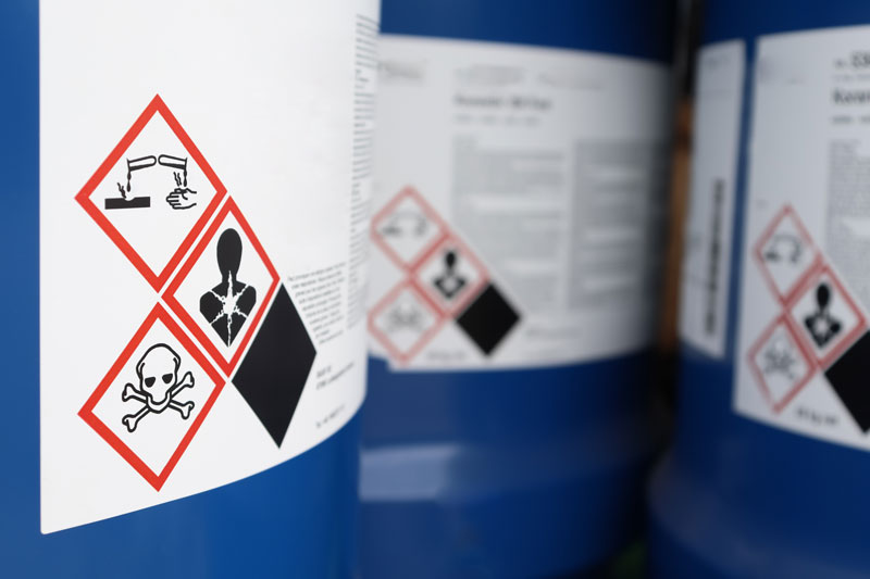 Close-up of chemical hazard warning labels on blue drums indicating various safety symbols.