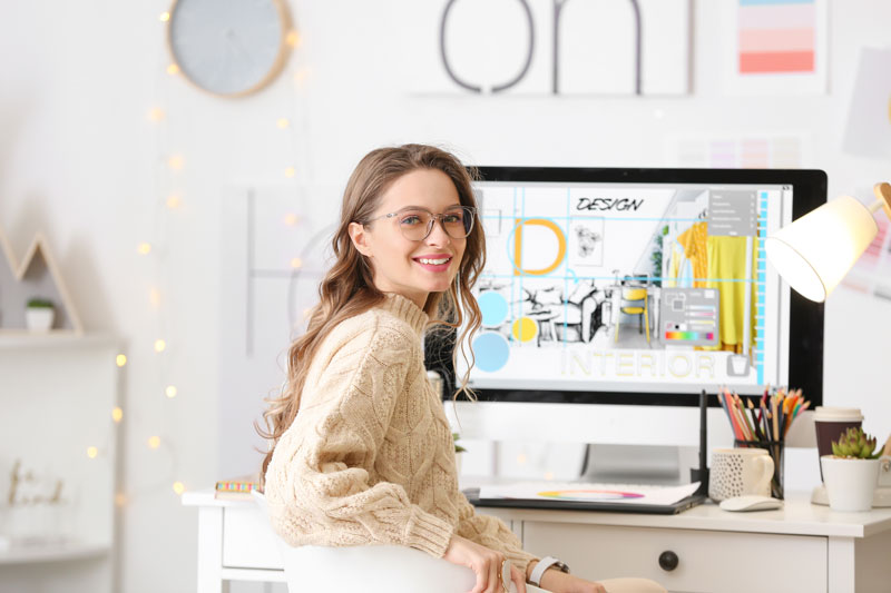 Graphic designer sitting at a desk with a computer displaying design elements and color palettes.