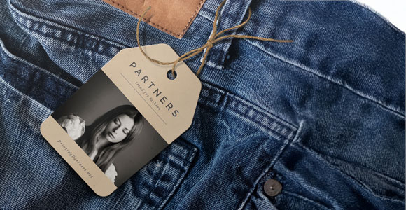 Hang tag attached to denim clothing featuring the word 'PARTNERS' and a black and white image of a woman.