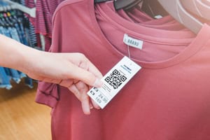 A hand holding a hang tag with a QR code attached to a maroon shirt.