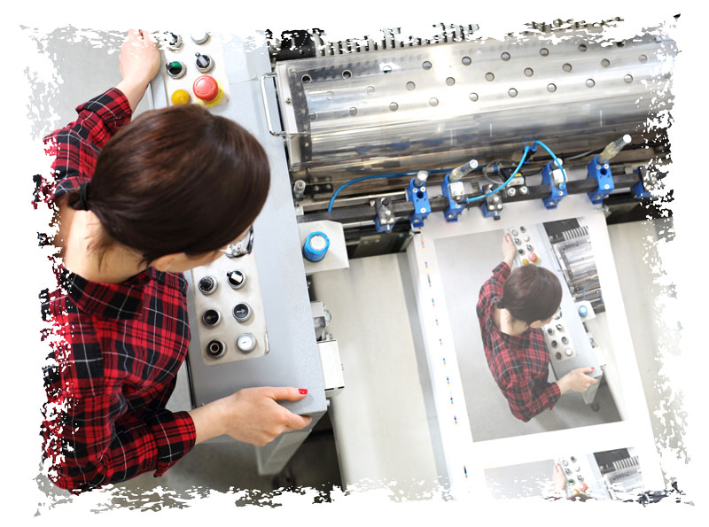 A printing machine operator adjusting controls while monitoring printed sheets in a printing facility.
