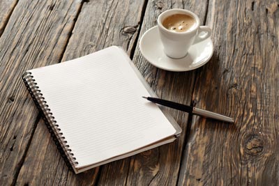 A blank spiral notebook next to a cup of coffee on a wooden table.