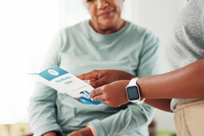 A person handing a leaflet to another individual who is seated, both appearing engaged in conversation.