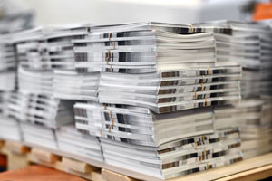 Stack of neatly arranged commercial printing magazines on a wooden pallet.