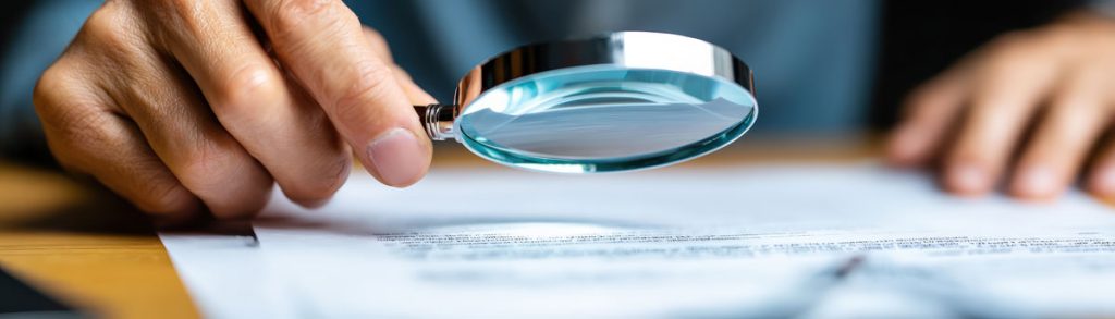 A person inspects a document closely using a magnifying glass to