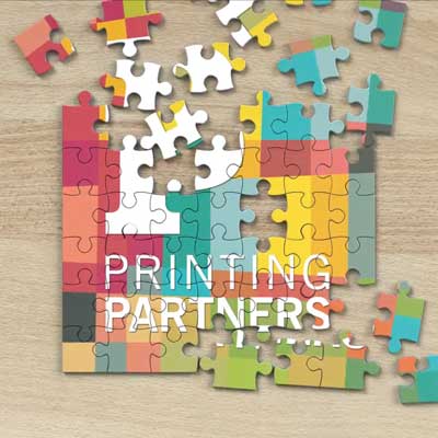 Colorful puzzle pieces arranged around a partially completed puzzle featuring the Printing Partners logo.