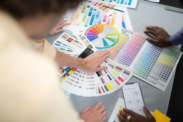 A collection of color swatches and a color wheel displayed on a table with hands reaching for them.