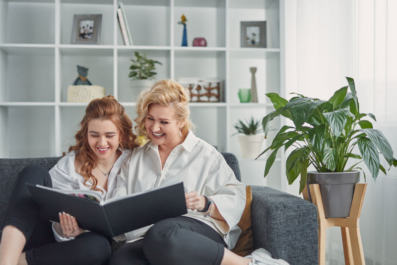 Two women sitting on a couch, looking at a coffee table book together.