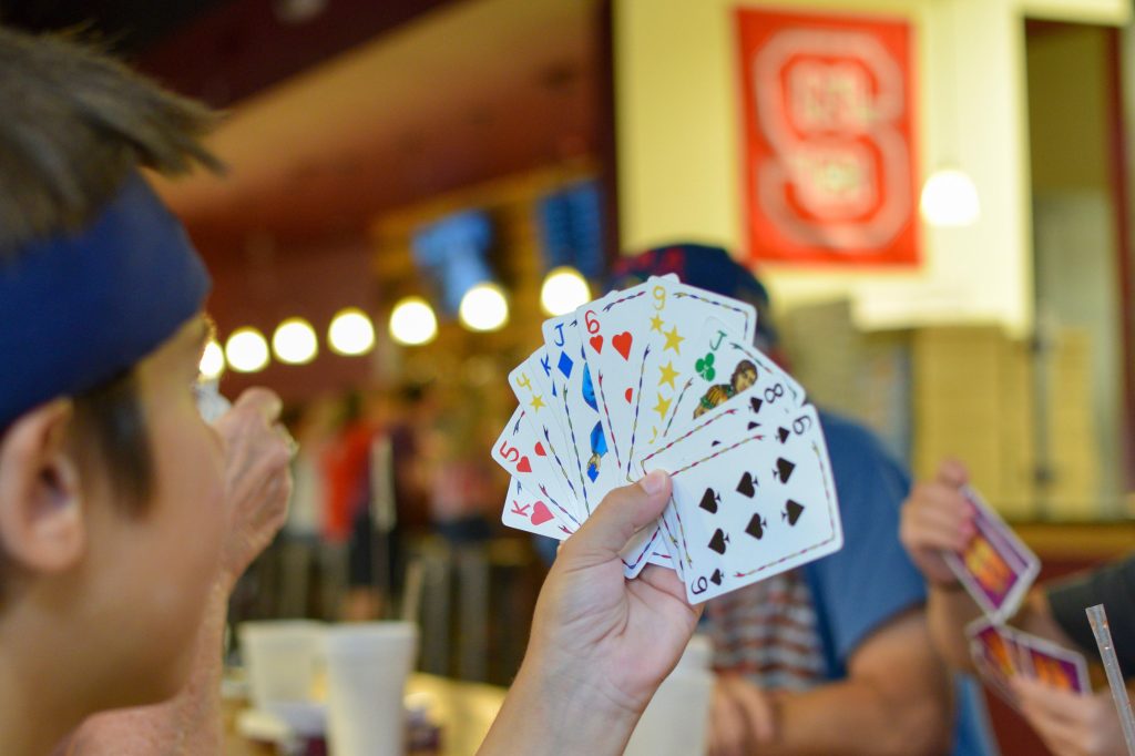 Child holding a hand of playing cards while seated at a restaurant table.