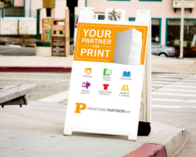 Outdoor A-frame sign displaying services offered by Printing Partners, including printing and graphic design.