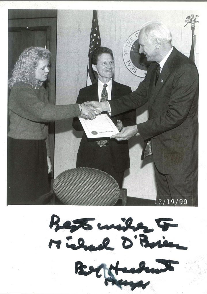 Black and white photo of a mayoral ceremony with two individuals shaking hands and a certificate being presented.