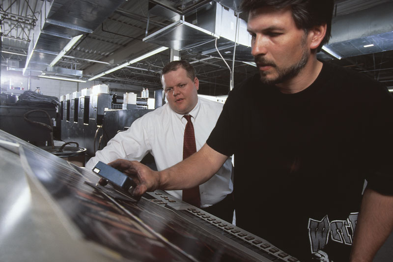 Two printing press operators working on a printing machine in a production facility.
