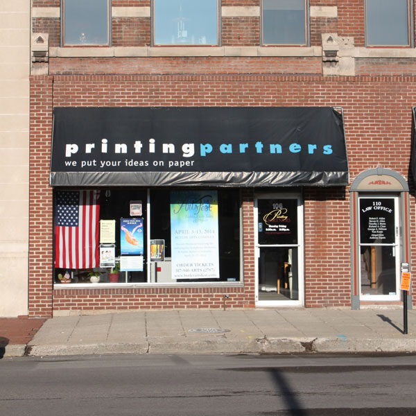 Exterior view of Printing Partners storefront with a sign and American flag.