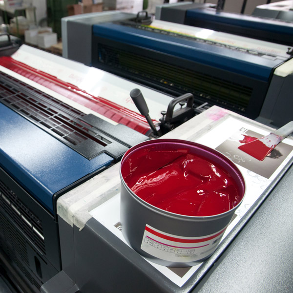 A container of red ink placed on a printing press with a brush beside it.