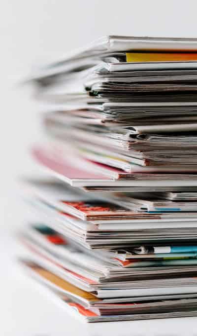 Stack of printed materials including magazines and brochures in various colors and sizes.