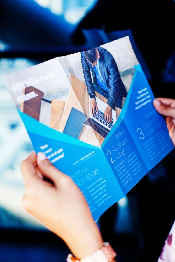 A person holding a blue brochure with text and images, displaying an informational layout.