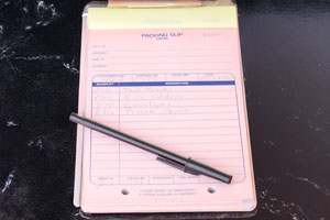 A pink carbonless form lies on a clipboard with a pen across it, matching the carbonless forms layout and recordkeeping focus on the page.