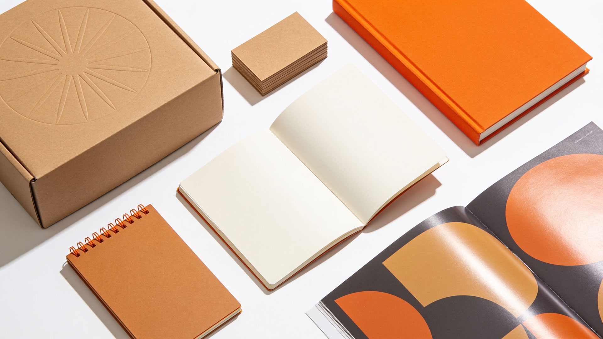 Flat lay of premium print work produced by Printing Partners: embossed kraft packaging, business cards, a wire-O bound notebook, and an open brochure on a white studio background