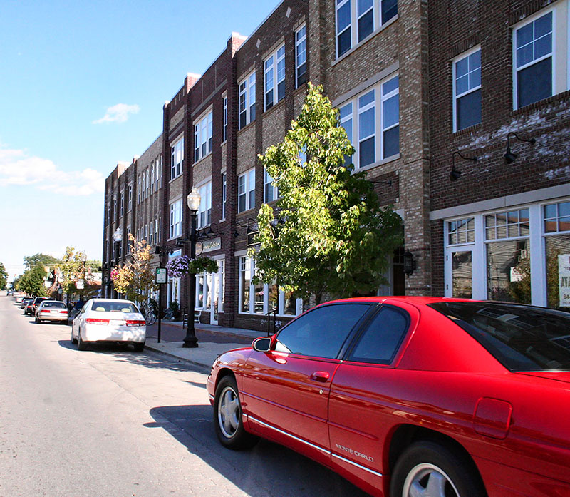 Street view in Downtown Carmel, Indiana featuring a red car parked alongside brick buildings.