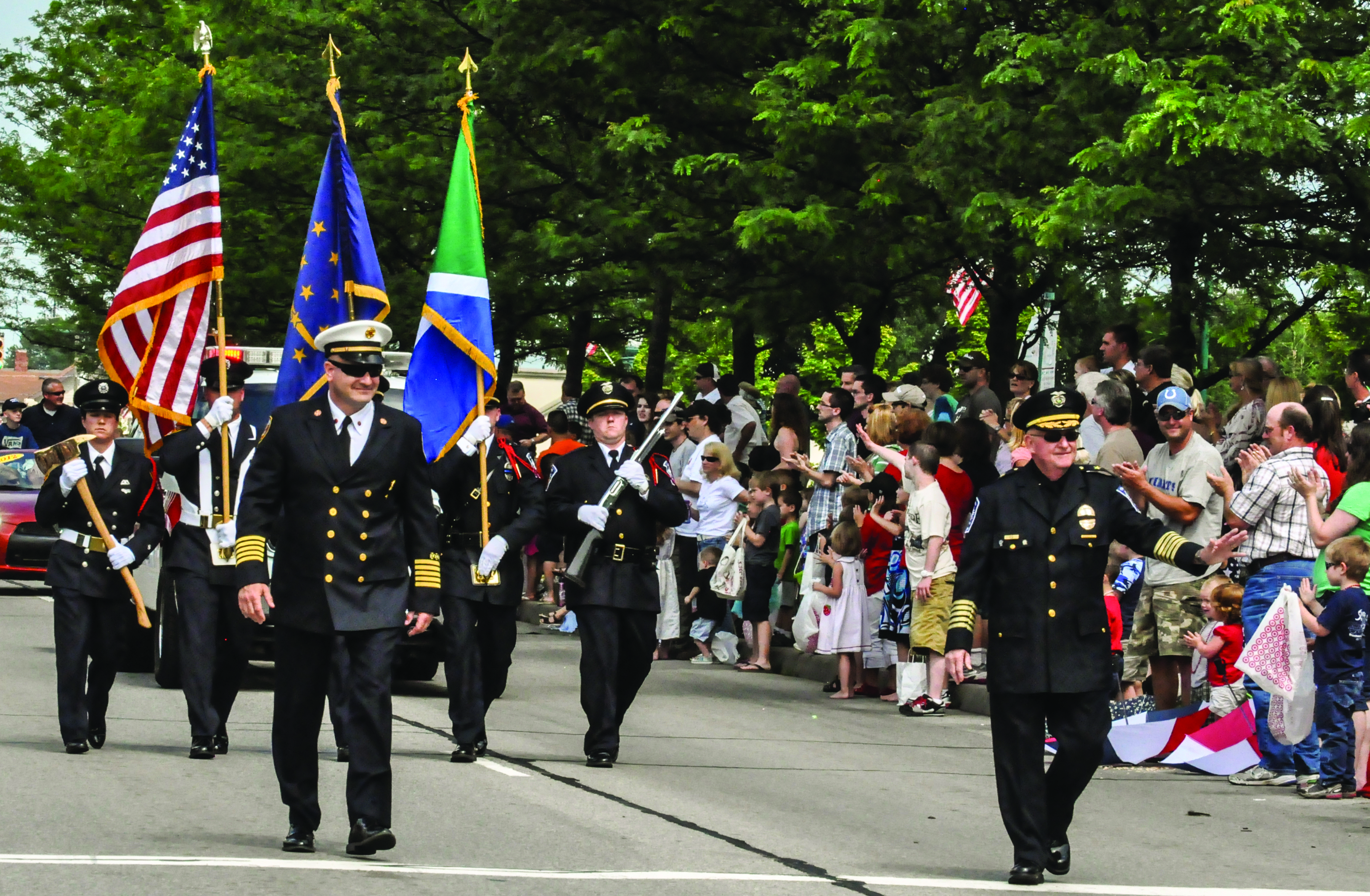 Color guard carrying American, Indiana, and other flags during a parade with spectators in the background.