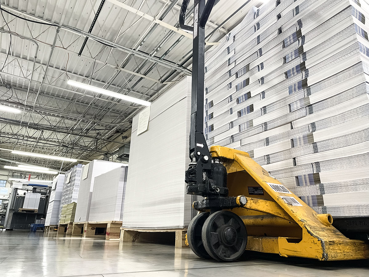 Printing Partners production floor at 929 W 16th Street in Indianapolis, with stacked paper pallets and a yellow pallet jack.