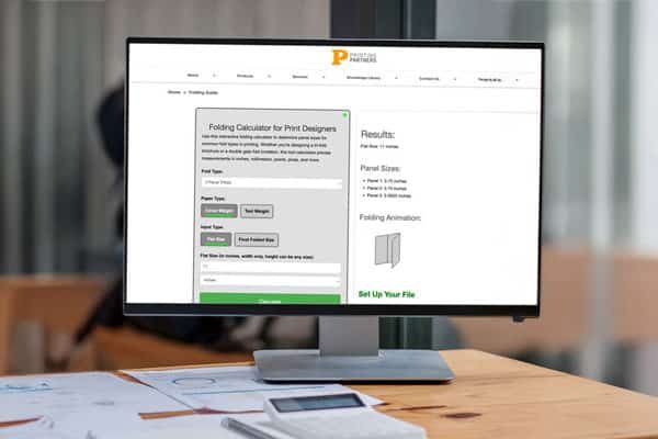 Close up view of simple workspace with open blank screen laptop, frame and notebook on white table with blurred office room background Close up view of Printing Partners Folding Calculator, notebook on white table with blurred office room background.