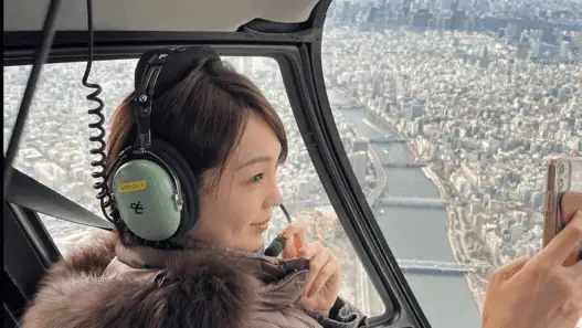 Helicopter soaring over Tokyo skyline with Mount Fuji in the distance.