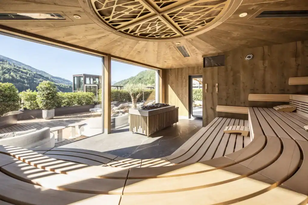 Luxury wellness retreats 2025 - Quellenhof Resort modern sauna with panoramic Alpine views, curved wooden benches, and mountain landscape for European medical excellence programs