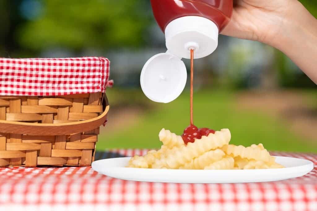 Creamy potato salad with cherry topping on a white plate, outdoor picnic setting.