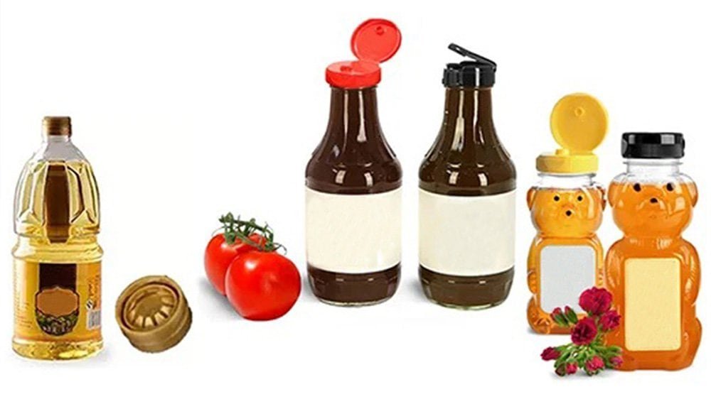 Golden syrup bottle with cap, fresh tomatoes, condiment bottles with bear-shaped lids, and herbal medicine jars, all on a plain white background, highlighting kitchen essentials and food storage options.